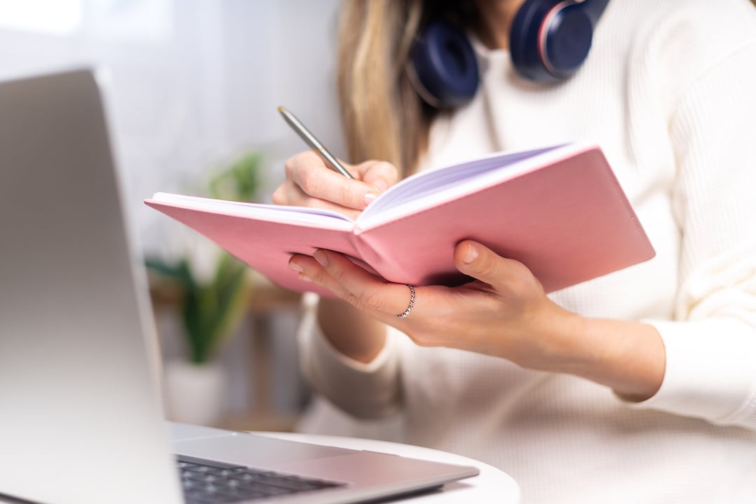 Woman writes in notebook with laptop